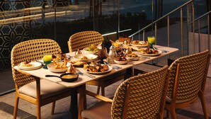 Una mesa de comedor dispuesta con diferentes platos, vasos y cubiertos, rodeada de sillas de mimbre.