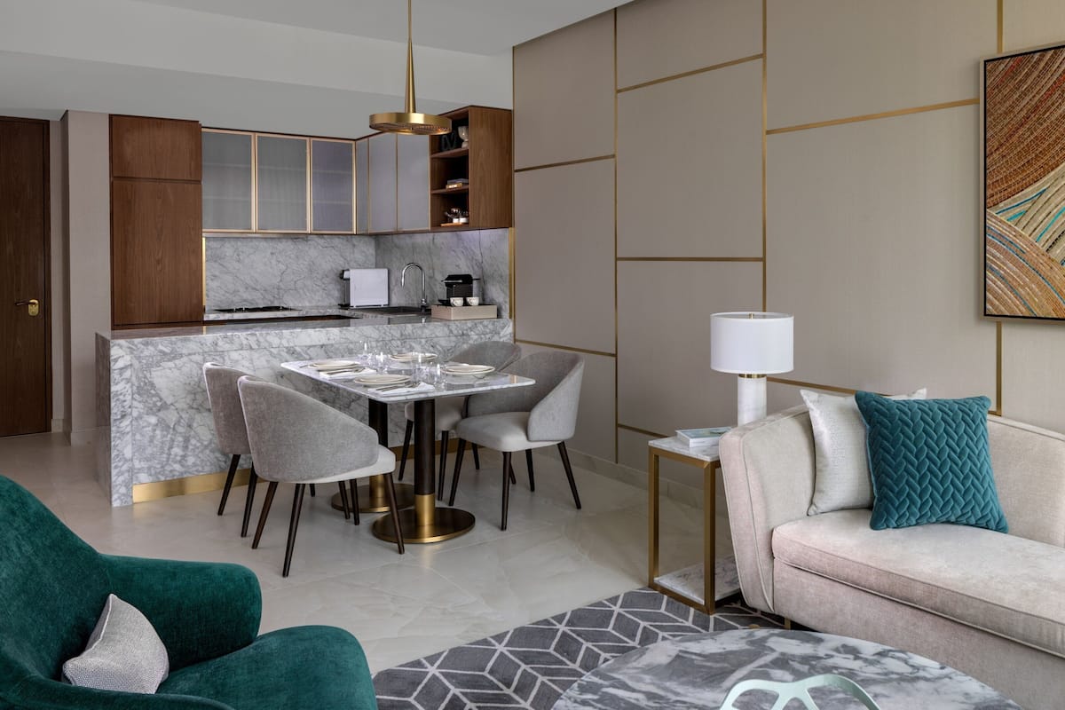 Een moderne woonkamer met een bank, een eettafel voor vier personen en een keuken met houten kastjes en een marmeren aanrecht.