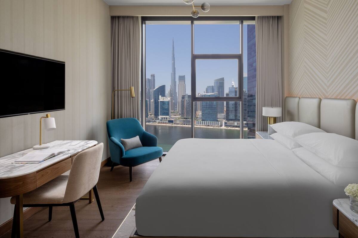 Een hotelkamer met een groot bed, een bureau met stoel, een televisie en uitzicht op een stadszicht.