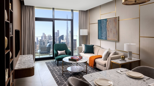 Habitación de hotel moderna con vista a la ciudad, un sillón verde, un sofá, una zona de comedor y un cuadro grande en la pared.