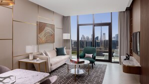Una habitación de hotel moderna con vista a la ciudad, un sofá, un sillón verde, una mesita y un televisor.