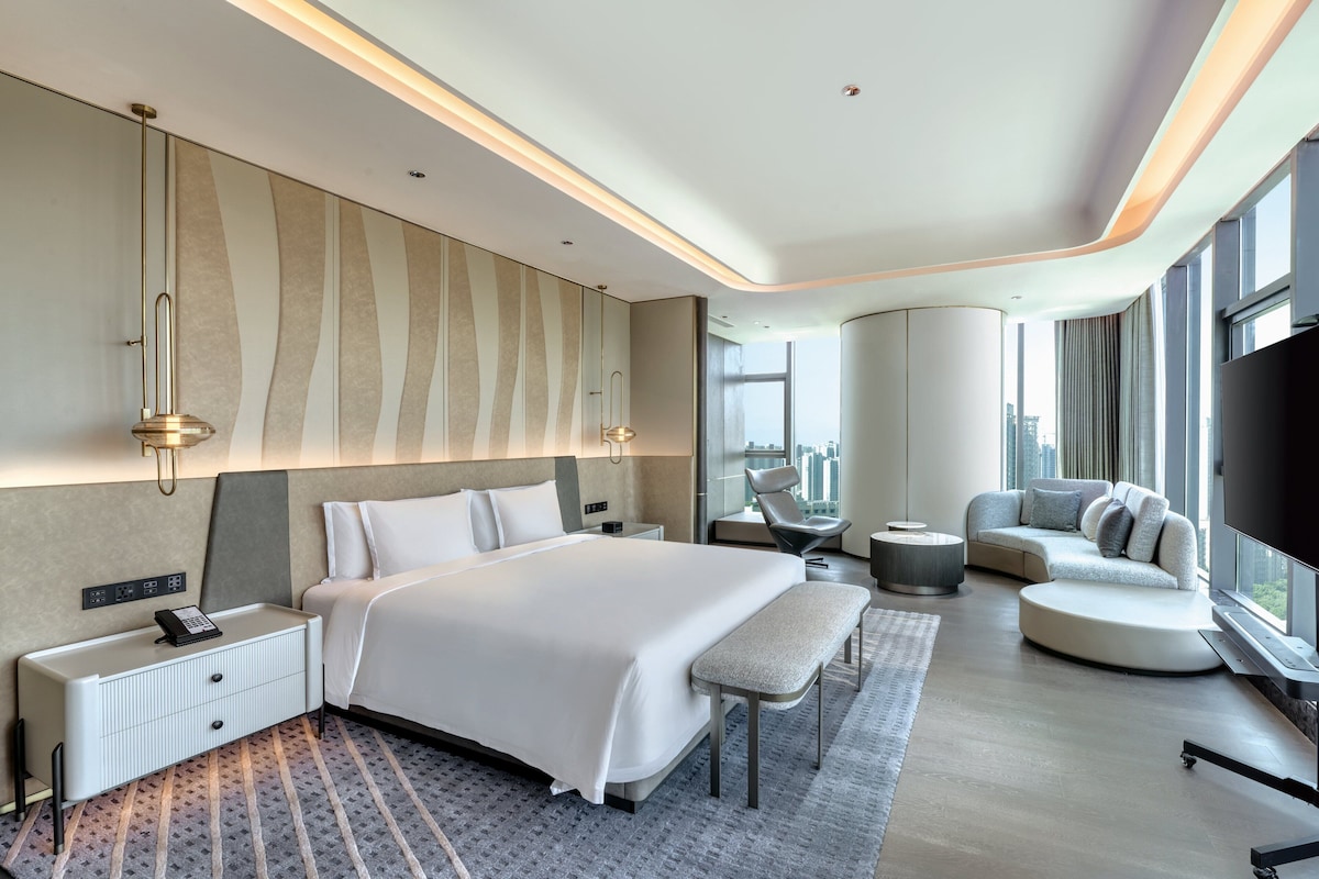 A modern hotel room with a large bed, a seating area, and a city view.
