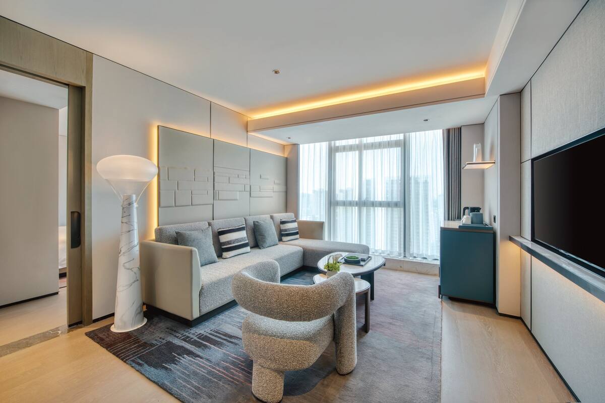A modern living room with a sofa, a coffee table, a TV, and a large window.