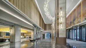 Um hall amplo com design moderno, apresentando um longo corredor, uma área de recepção e um espaço de estar com vista para o exterior.