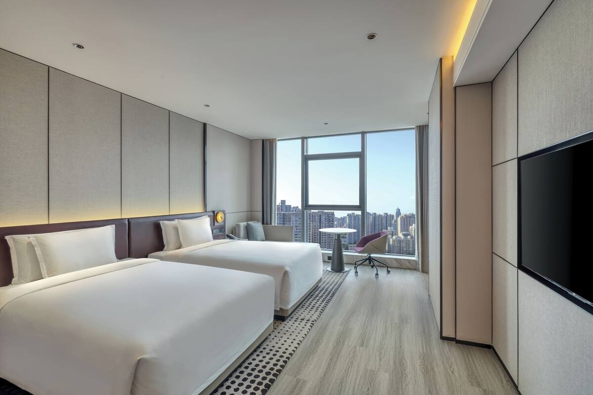 A modern hotel room with two beds, a TV, a small table, and a chair.