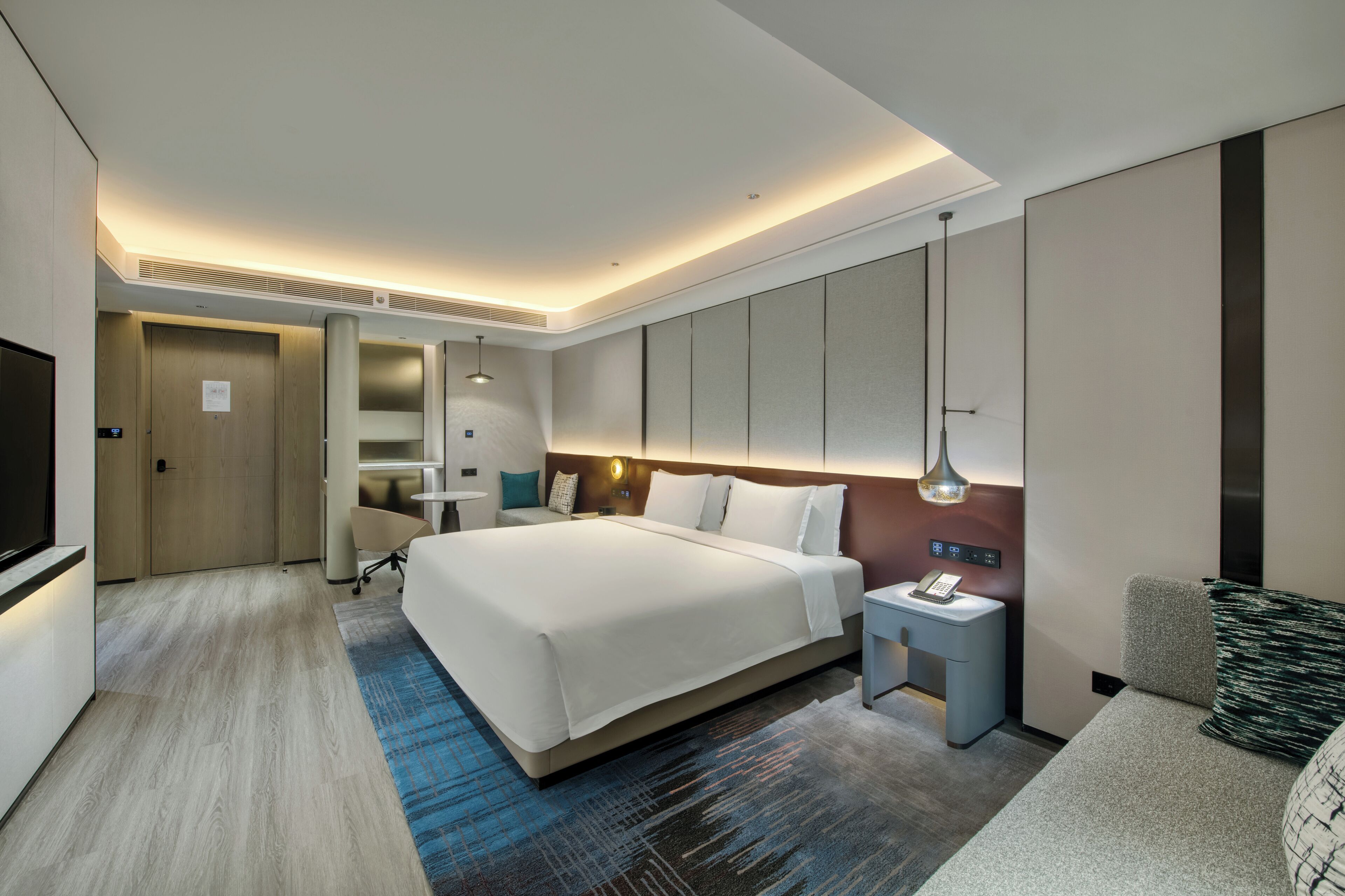 Una habitación de hotel moderna con una cama grande, mesitas de noche, un escritorio y un televisor.