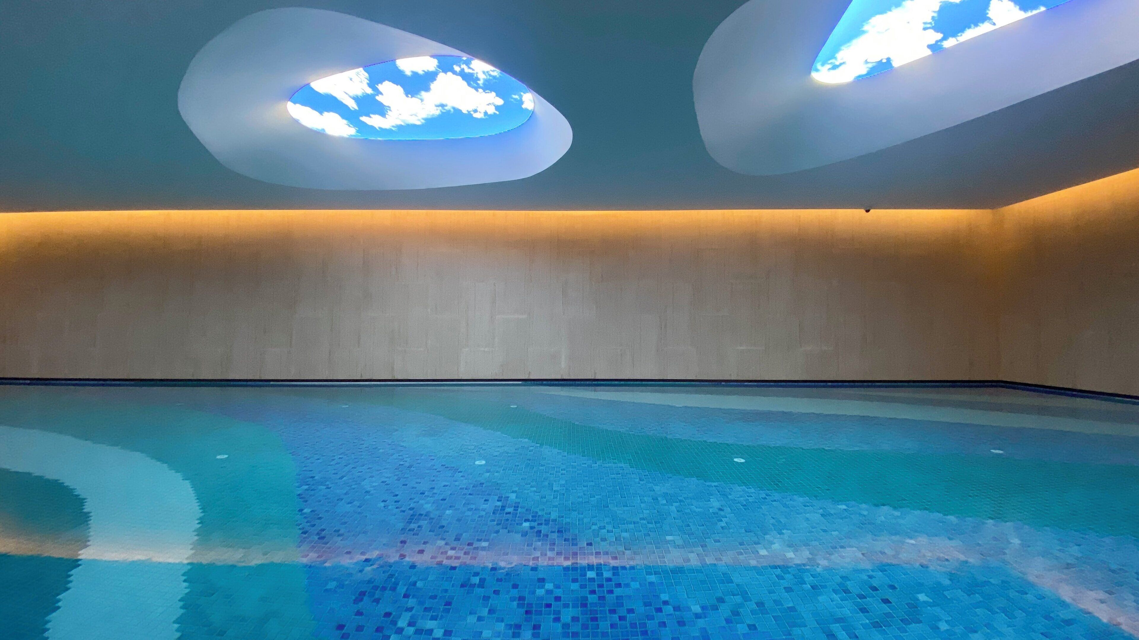 A swimming pool with a tiled floor and a ceiling with two illuminated cloud-shaped lights.