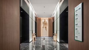 En modern hotellobby med ett marmorgolv, ett centralt placerat konstverk på väggen och en informationsskylt som listar bekvämligheter som ett fitnesscenter, en restaurang och en parkeringsplats.