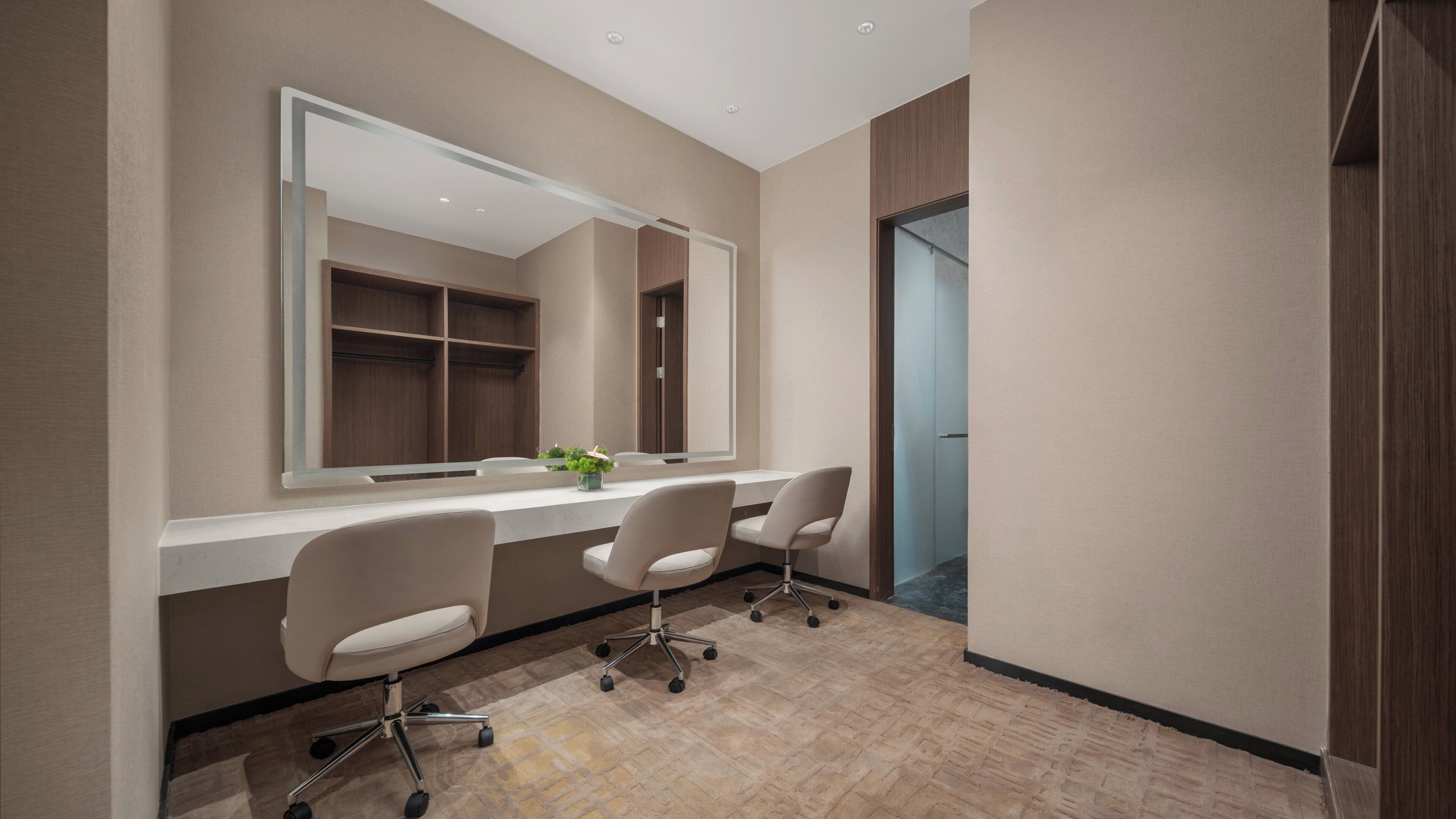 A modern bathroom with a large mirror, two chairs, a vanity, and a wooden cabinet.