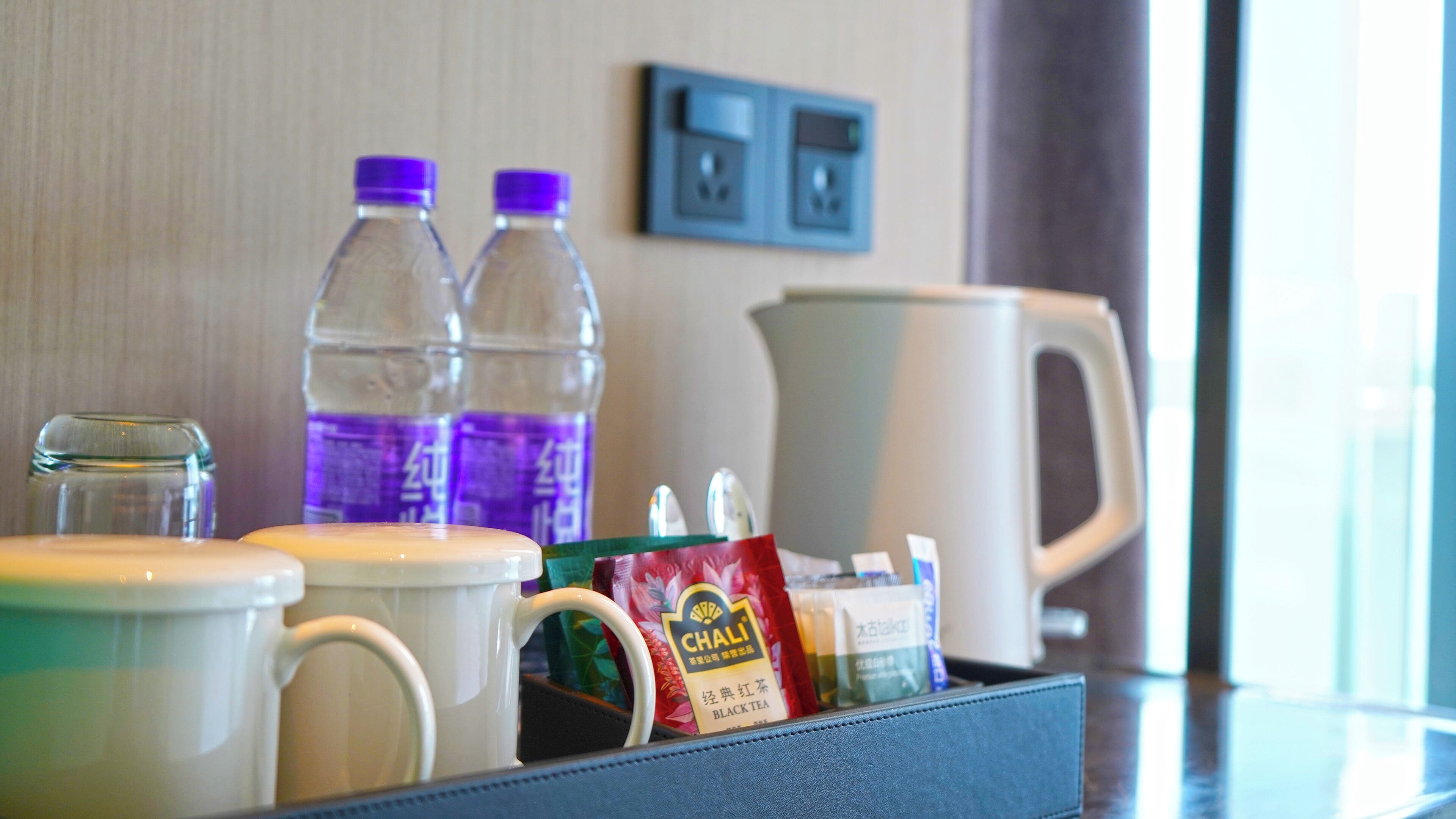 Ontbijtruimte in een hotelkamer, met een koffiezetapparaat, twee waterflesjes, een mok, een theezakje en een glazen pot.