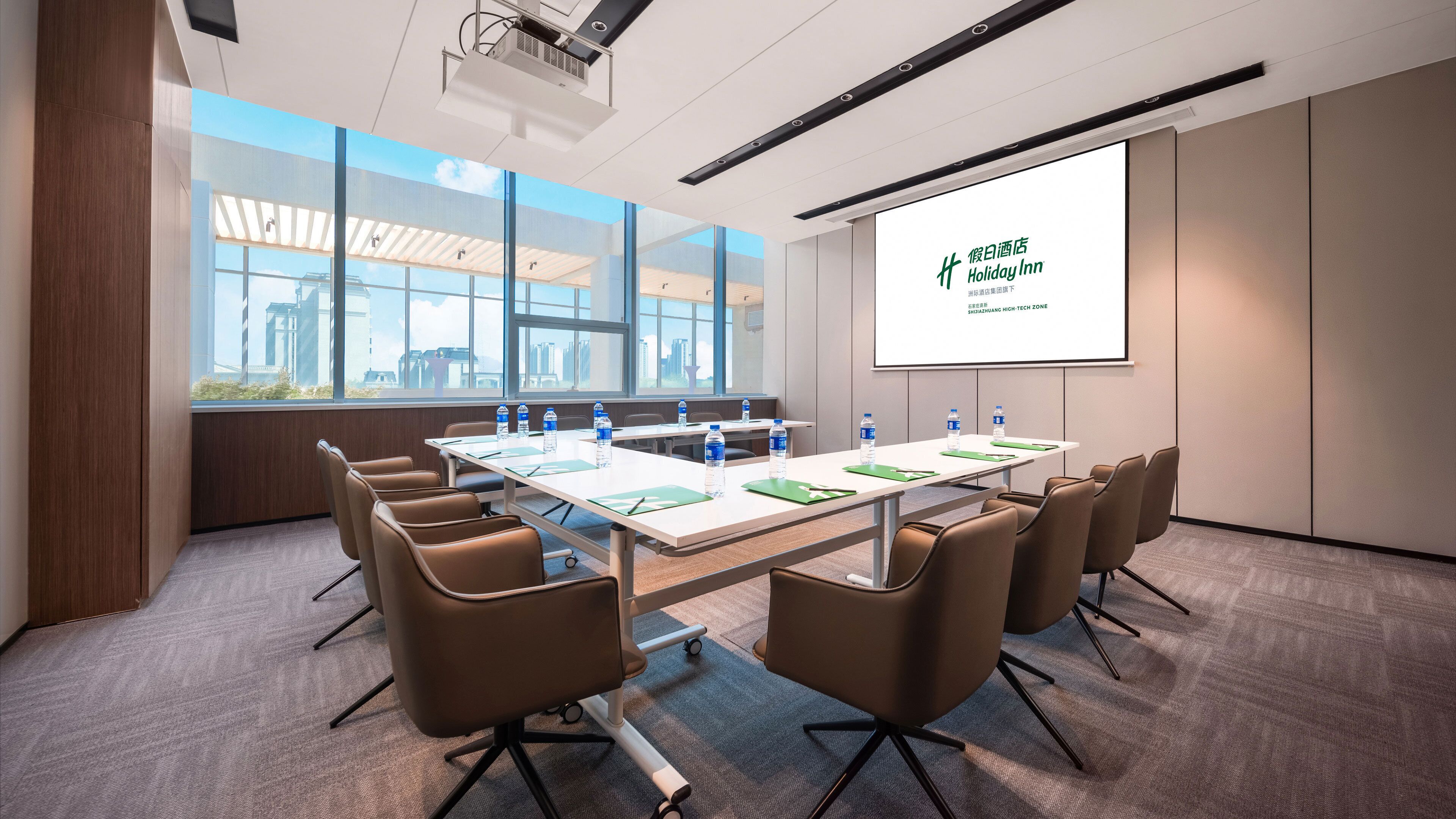 A conference room with a large table, chairs, a projector screen, and a view of the city through large windows.
