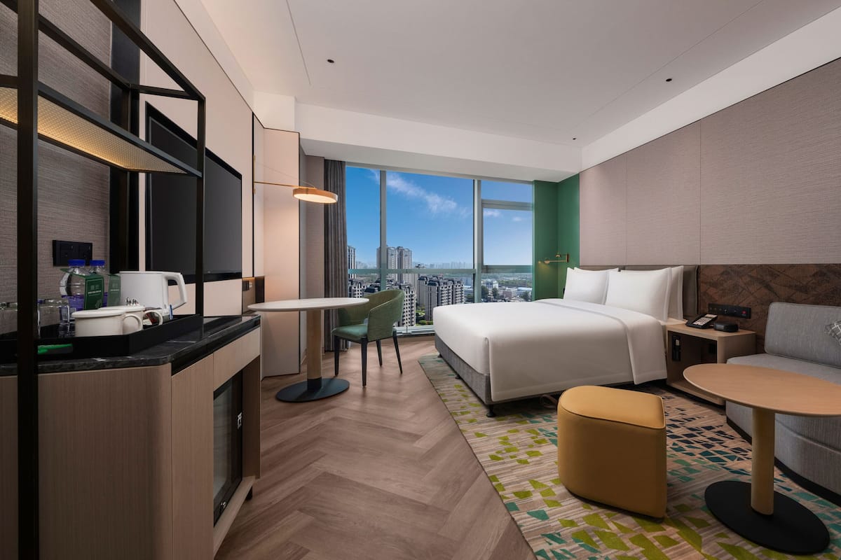 A modern hotel room with a bed, sofa, dining table, and kitchenette.