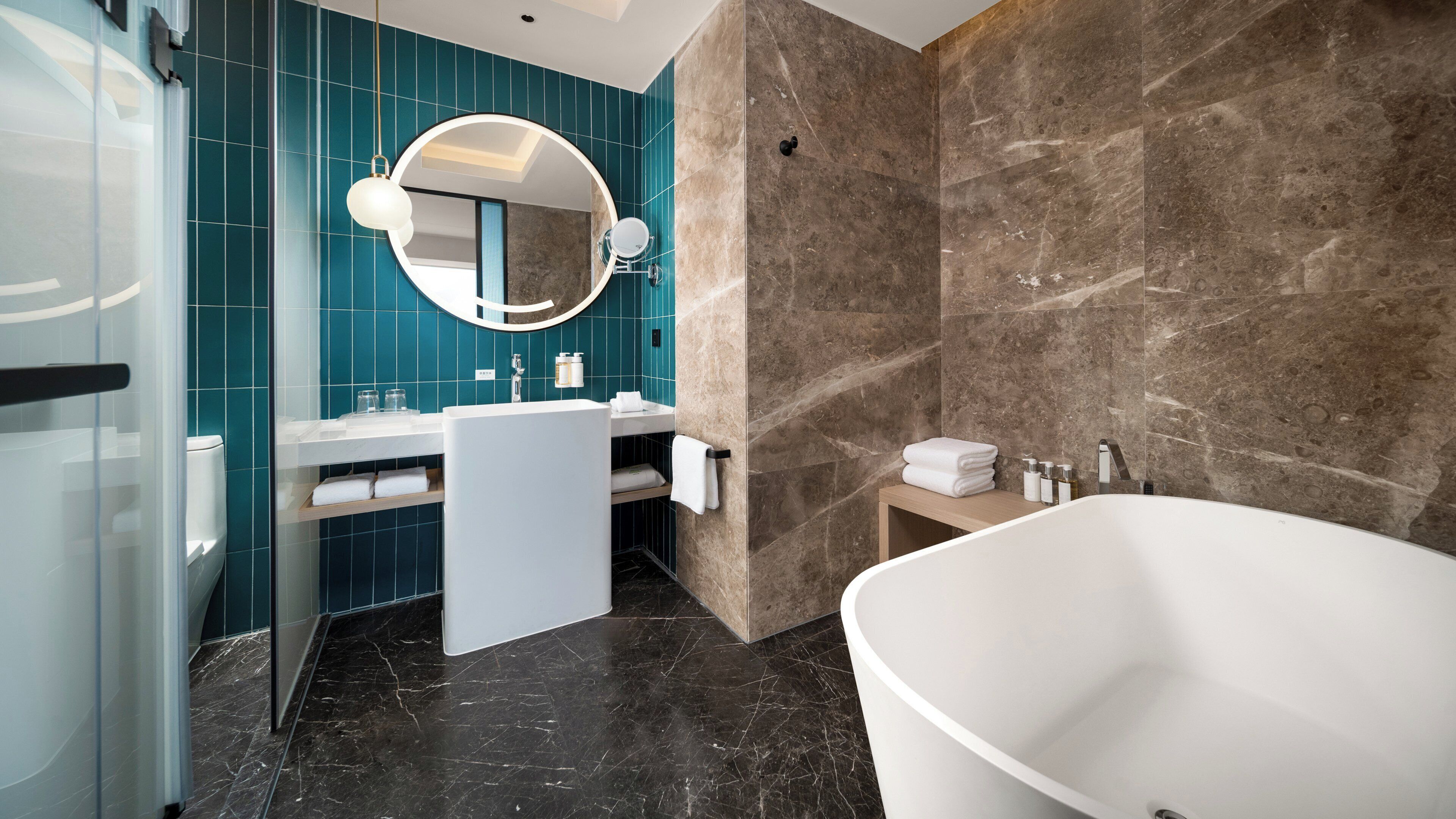 A modern bathroom with a freestanding bathtub, a round mirror, and a vanity with a sink and towel rack.