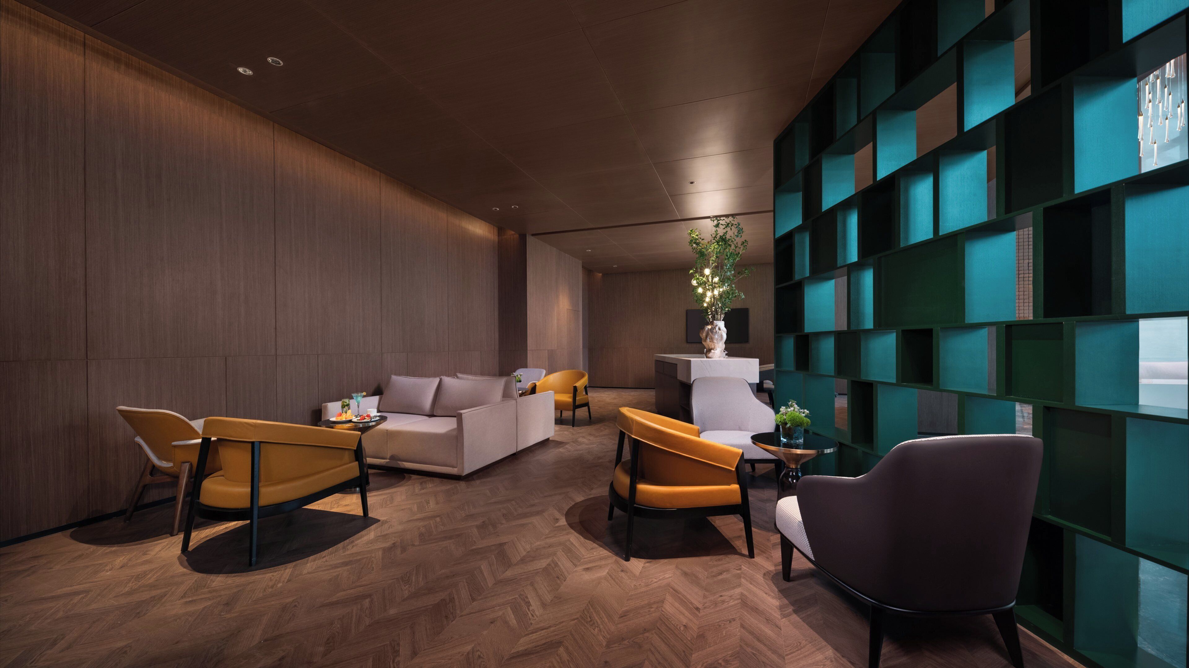 Un vestíbulo moderno con suelo de madera tipo espiga, un sofá, dos sillones, una mesa de centro y una planta decorativa.