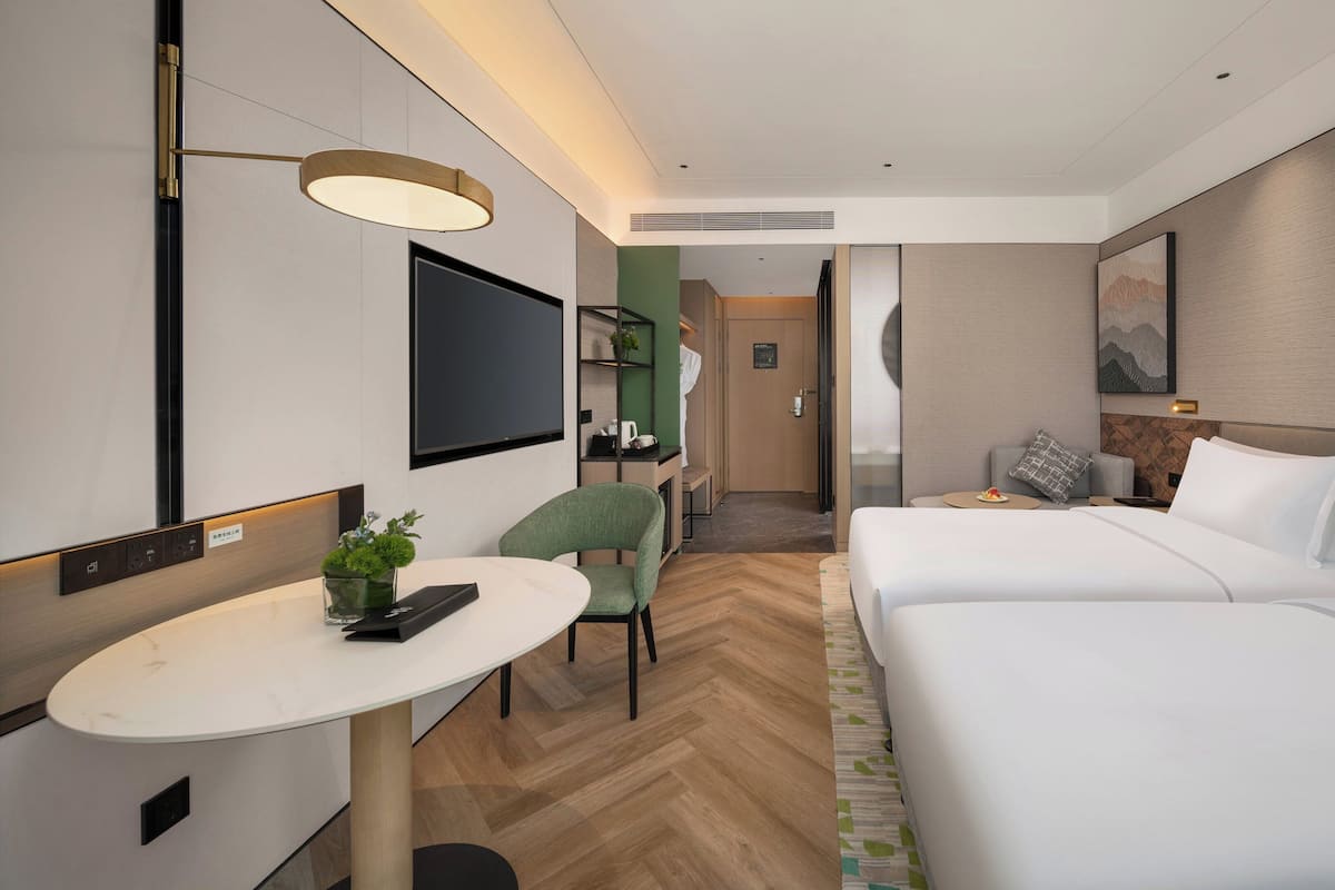 A hotel room with a bed, a desk with a chair, a TV, and a small table with a plant.