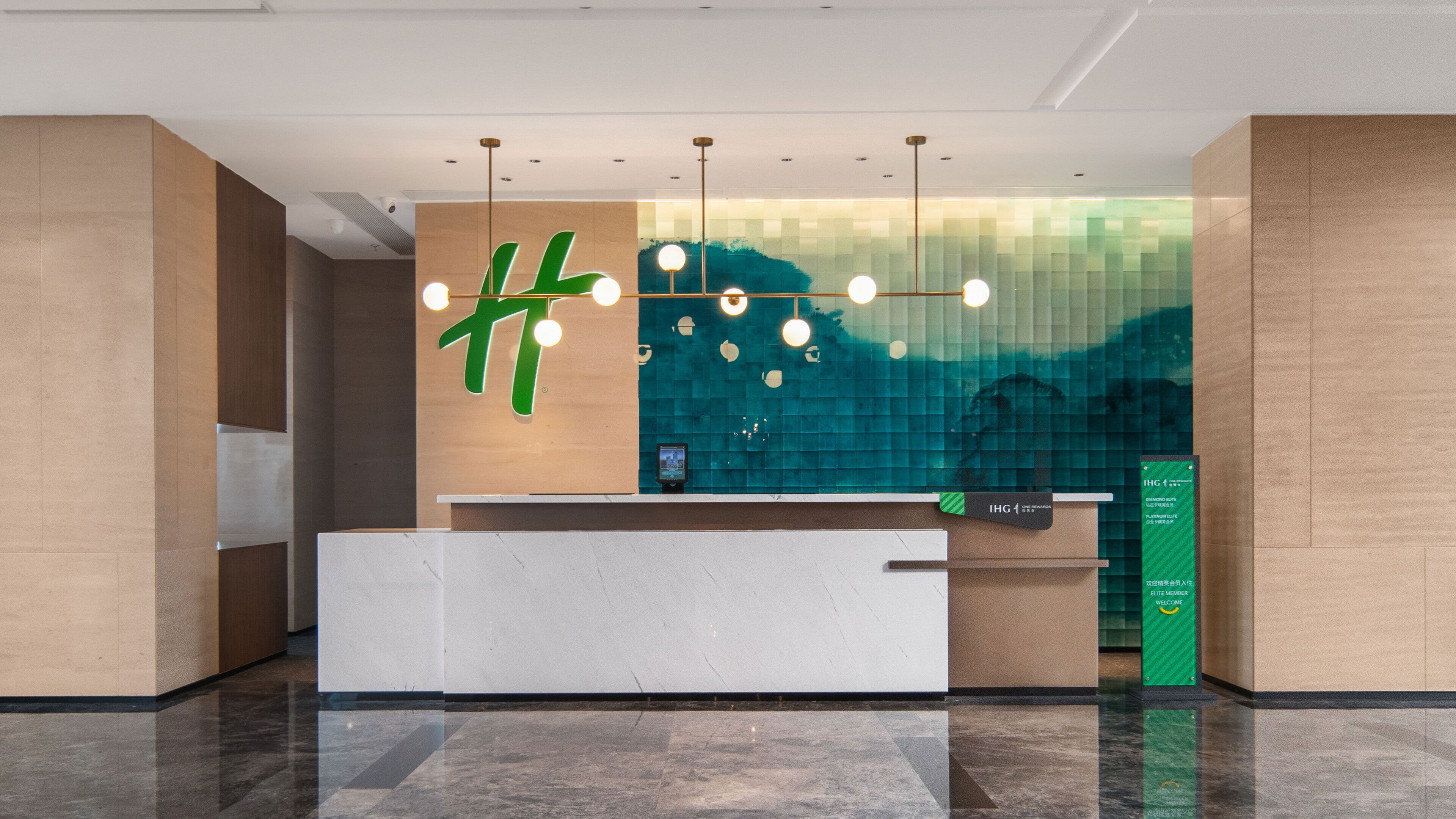 A reception desk with a modern design, a large green sign, and a digital screen.