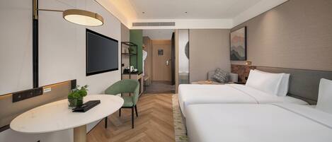 A hotel room with a bed, a desk, a chair, a TV, and a small table with a plant.