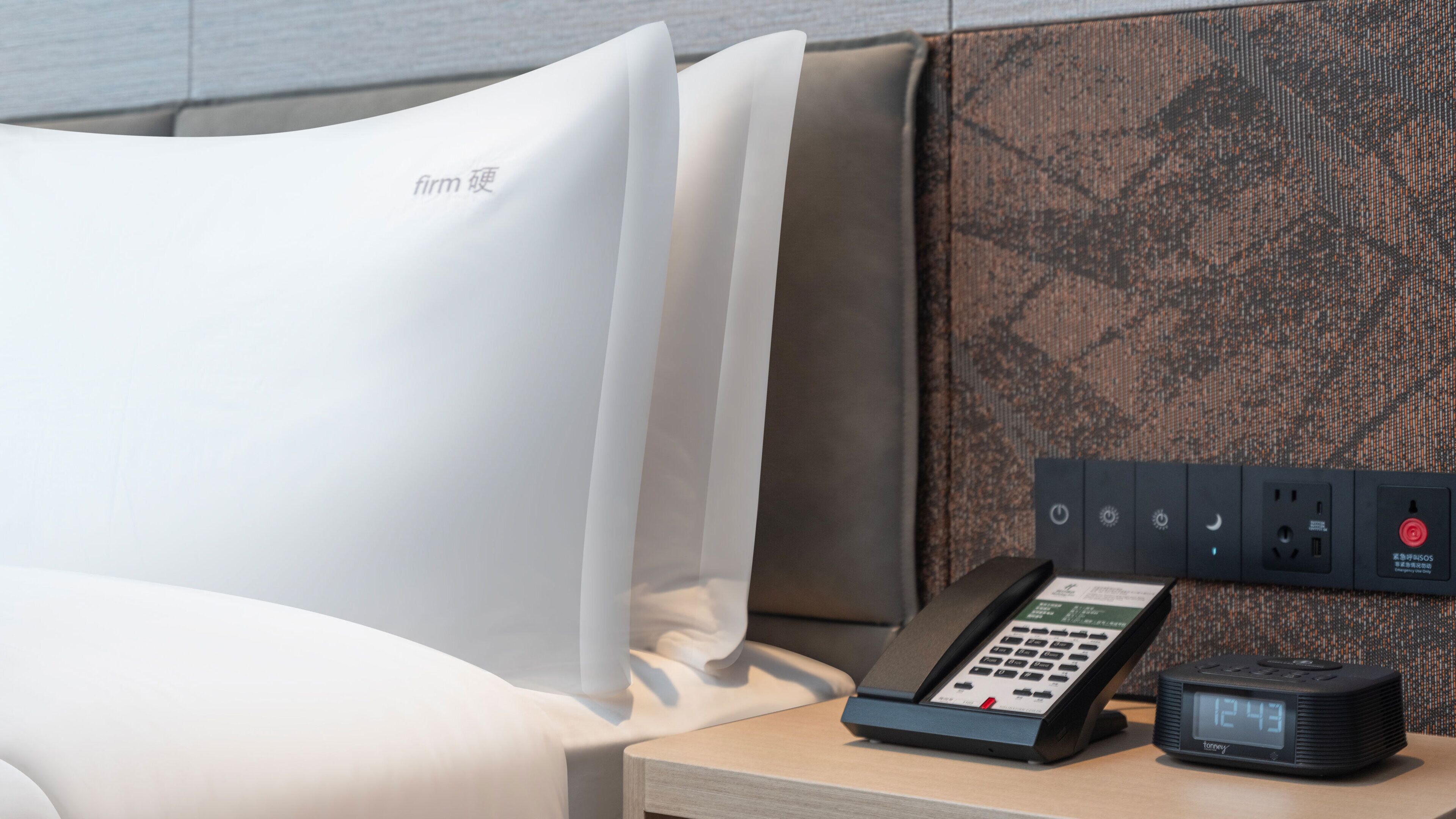 Une chambre d’hôtel équipée d’un lit, d’une table de chevet, d’un téléphone et d’une multiprise avec plusieurs prises.