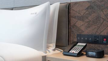 Une chambre d’hôtel équipée d’un lit, d’une table de chevet, d’un téléphone et d’une multiprise avec plusieurs prises.