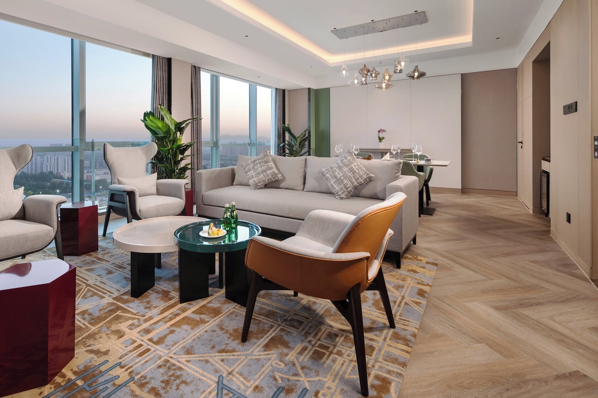 A modern living room with a sofa, chairs, a coffee table, and a dining area with chairs and a table.