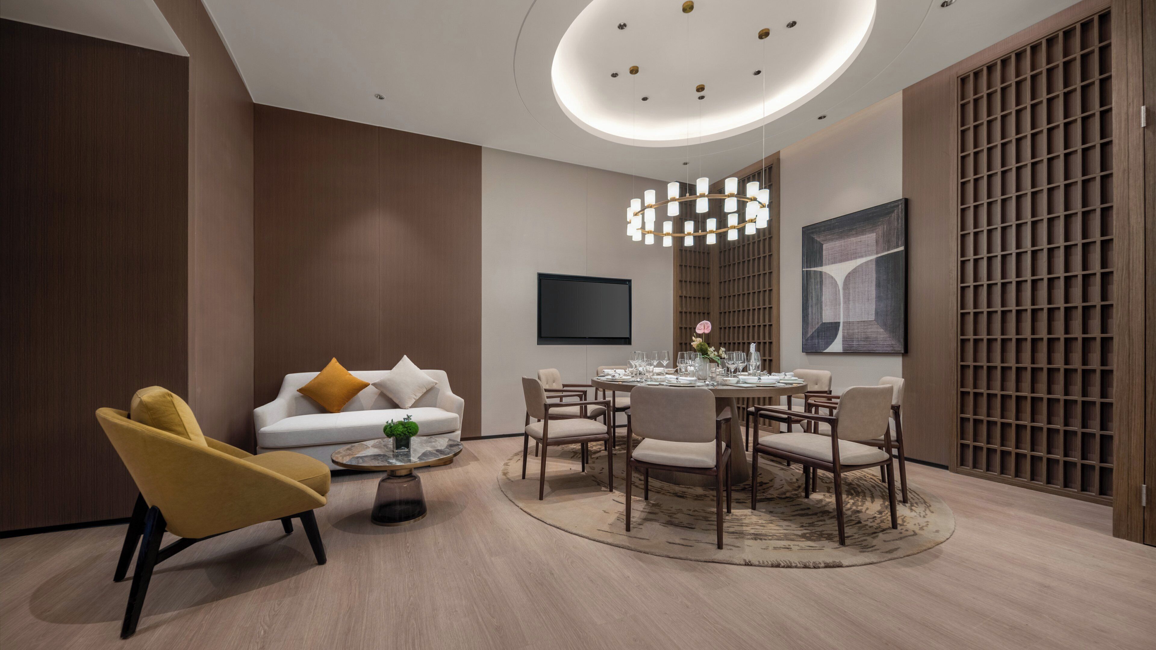 A modern dining area with a round table, chairs, a sofa, and a TV mounted on the wall.