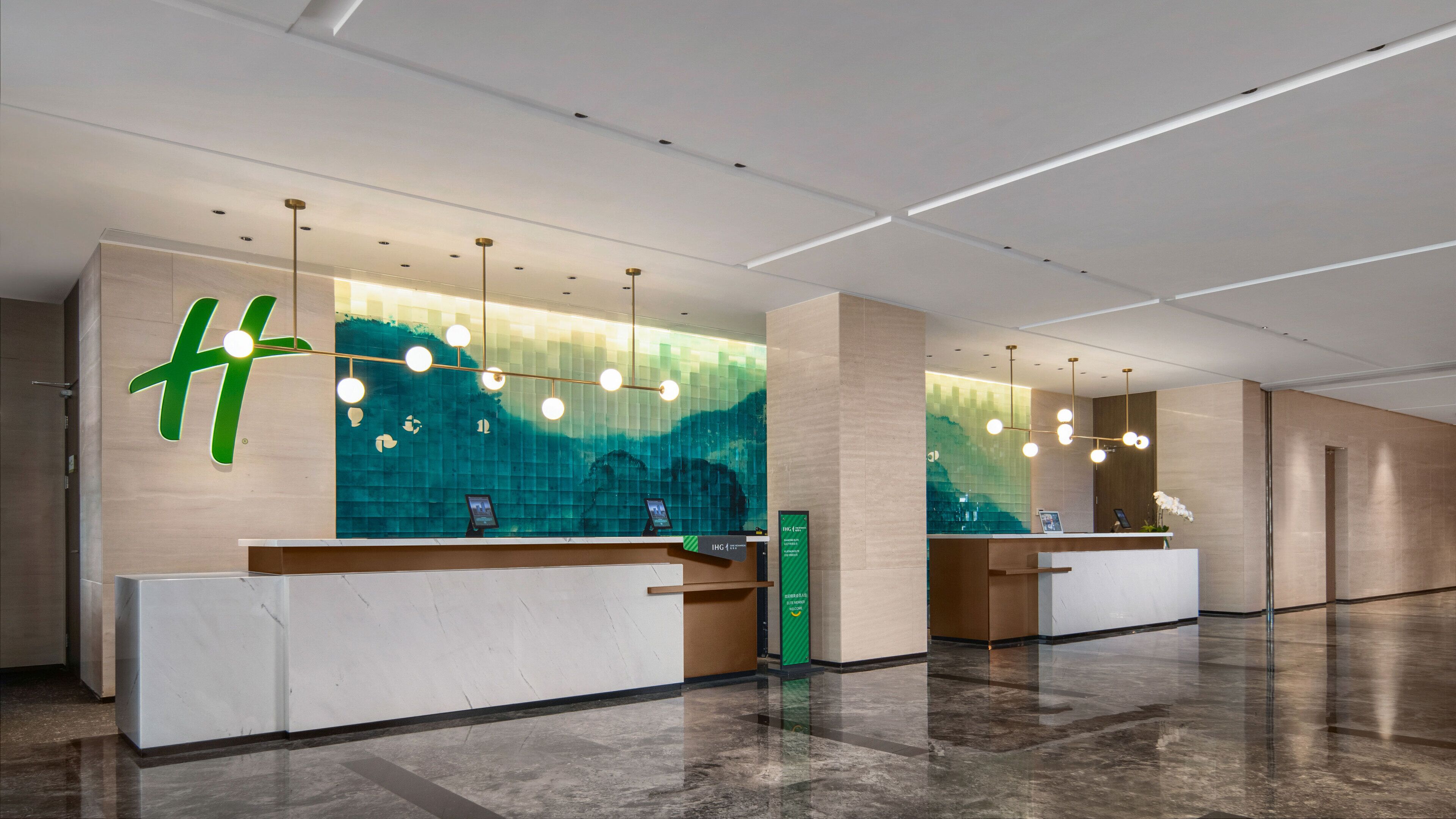A modern reception area with a large green logo, a digital information board, and a clean, polished floor.