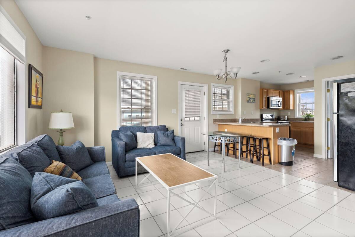 Una cocina moderna con una isla central, un área de comedor con una mesa y sillas, y una sala de estar con un sofá y una mesita de centro.