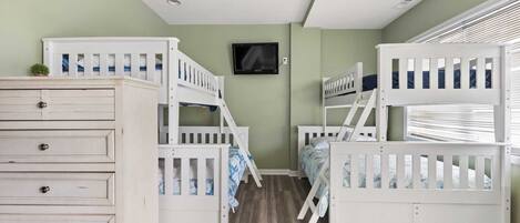 Una habitación infantil con literas, un aparador y un televisor en la pared.