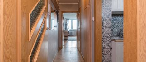 A hallway with wooden doors, a tiled floor, and a kitchen area with patterned tiles.
