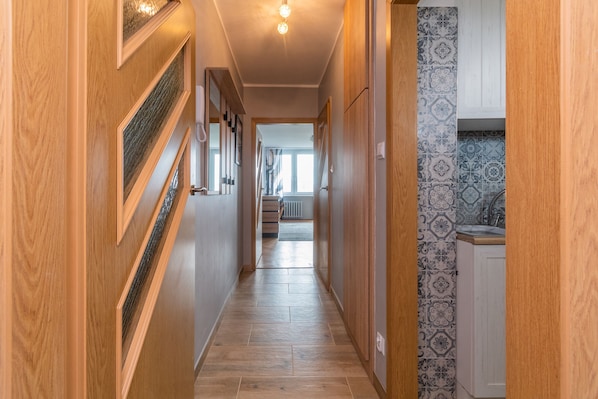 A hallway with wooden doors, a tiled floor, and a kitchen area with patterned tiles.