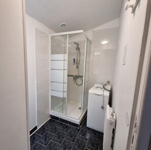 Een moderne badkamer met een glazen douchecabine, witte tegels en een klein wit kastje.