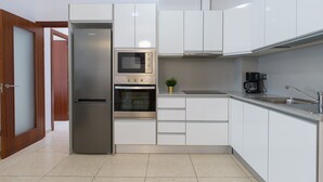 Cocina moderna con armarios blancos, electrodomésticos de acero inoxidable y piso de baldosas.