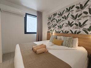 A hotel room with a large bed, a window with curtains, a wall with a leaf pattern, and a wooden headboard.