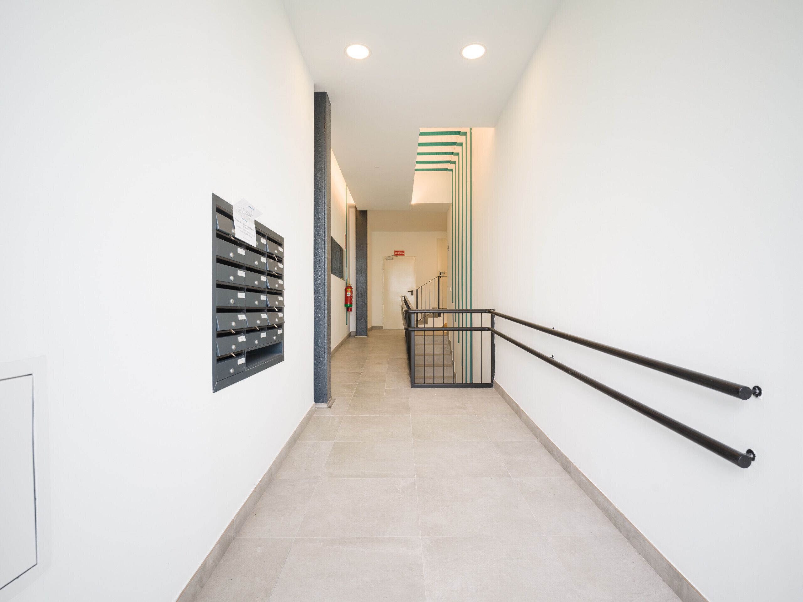 A clean, modern hallway with a fire extinguisher, a mail drop, and a staircase with black railings.