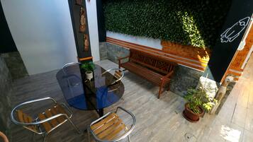 Un patio con una mesa redonda de vidrio, dos sillas de madera, un banco de madera y una planta en maceta.