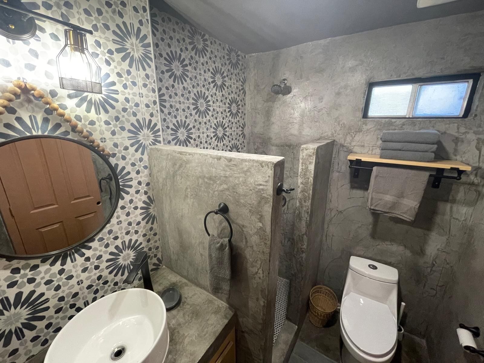 Ein Badezimmer mit rundem Spiegel, Waschbecken, Toilette, Dusche und Handtuchhalter.