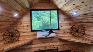 L’intérieur d’un chalet en bois, avec une grande fenêtre, des poutres apparentes et un luminaire au plafond.