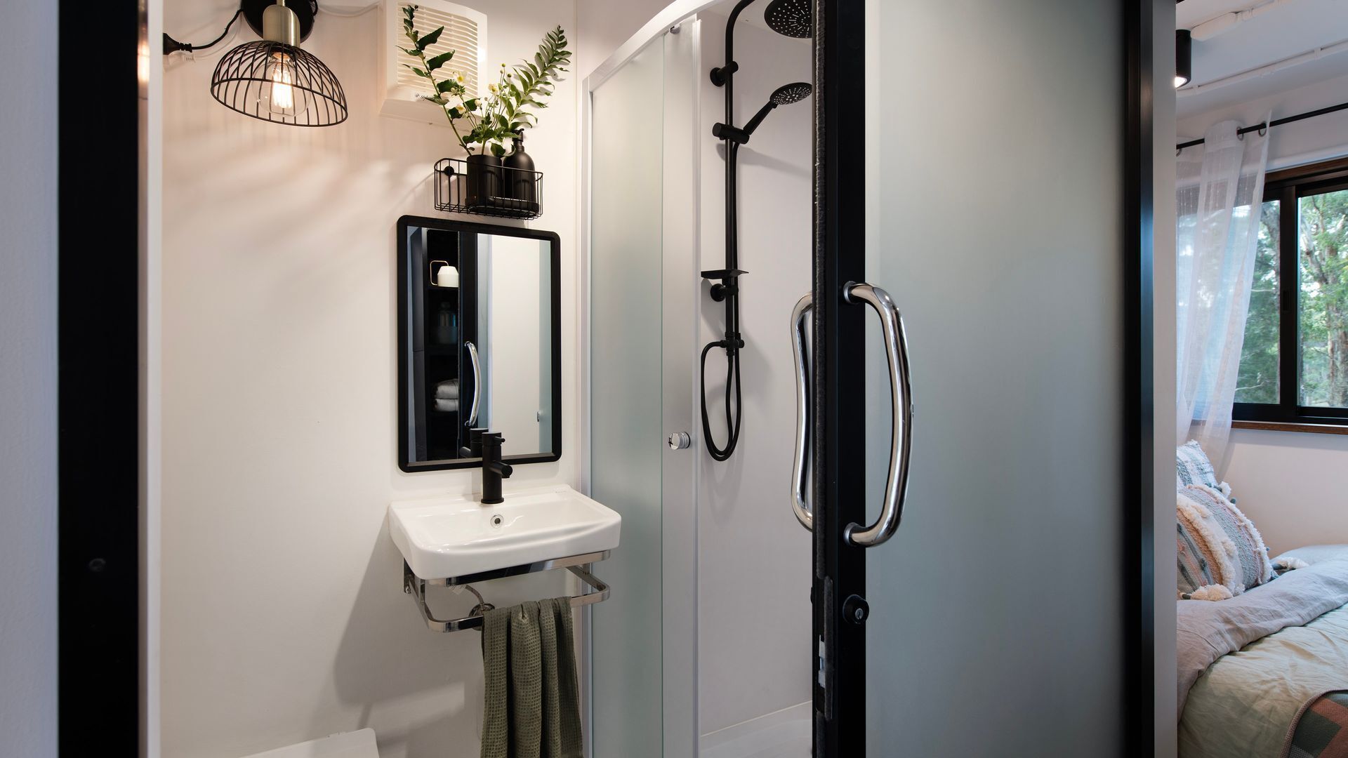 A bathroom with a white sink, a mirror, a shower with a handheld showerhead, and a towel rack.