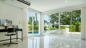 A modern room with a large glass door leading to a pool area, a desk with a chair, and a television on the wall. - Exclusive beach apartment with Wonderful View (Ko Lanta Yai)