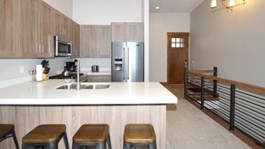 A modern kitchen with wooden cabinets, stainless steel appliances, and a central island with stools. - Adventure Awaits at R202 | Ridge Haven in Eden, UT! (Eden)