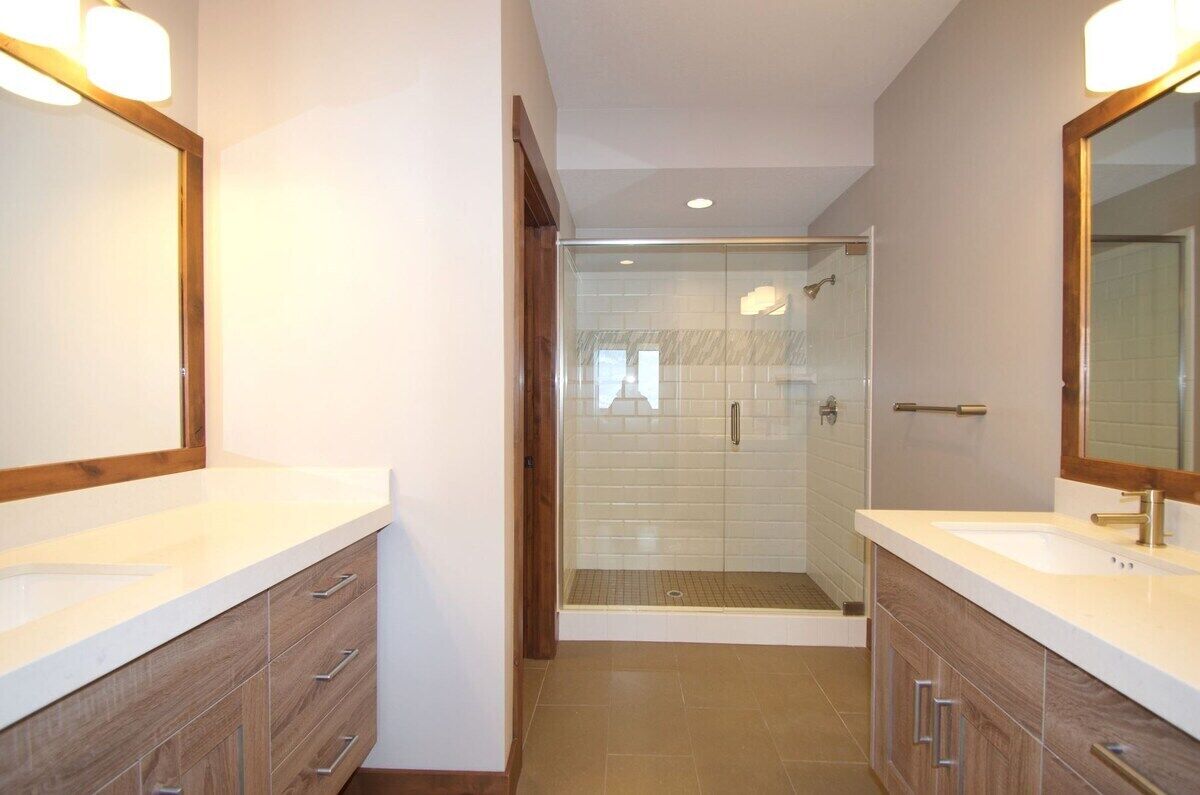Un baño moderno con dos lavamanos, muebles de madera y ducha con mampara de vidrio.