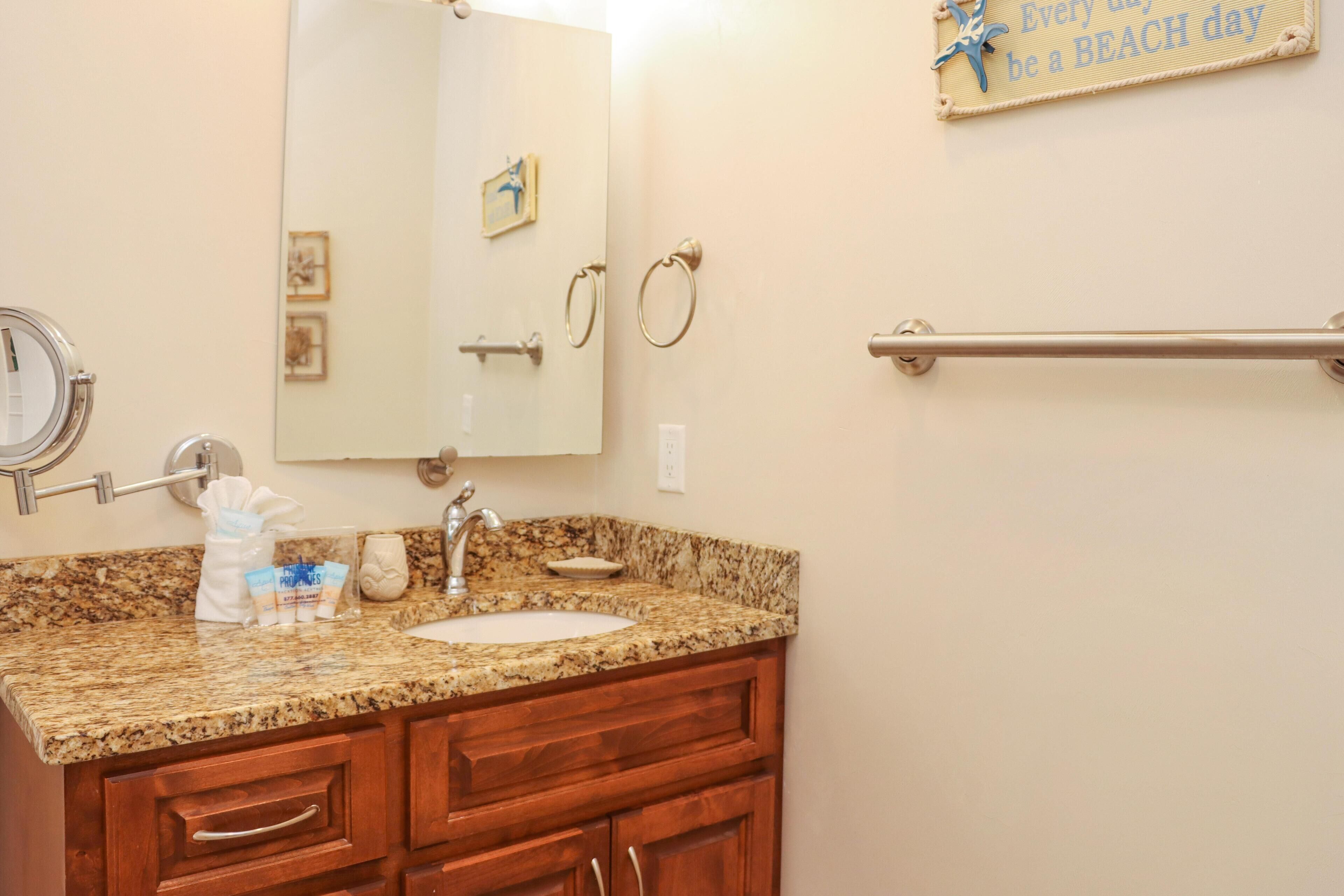 A bathroom with a granite countertop, a sink, a mirror, and a towel rack. There is a sign on the wall that says "Every day be a BEACH day."
