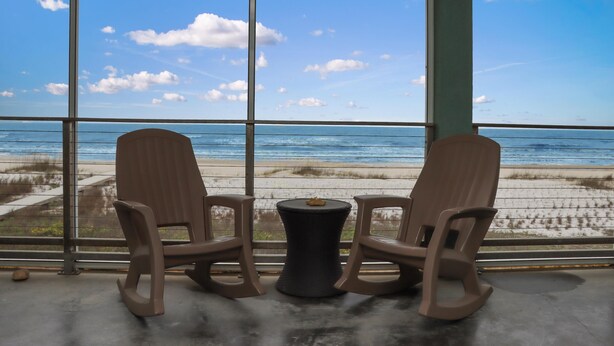 A room with a large window overlooking a beach, two rocking chairs, and a small round table. - Farr Away Living (Port St. Joe)
