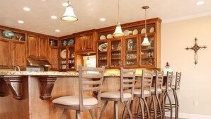 A kitchen with wooden cabinets, a granite countertop, and bar stools. - Farr Away Living (Port St. Joe)