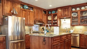 A kitchen with wooden cabinets, a stainless steel refrigerator, granite countertops, and a built-in dishwasher. - Farr Away Living (Port St. Joe)