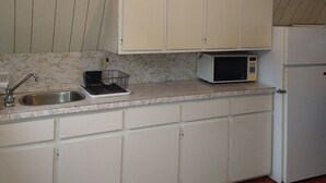 A small kitchen with white cabinets, a sink, a microwave, and a refrigerator.
