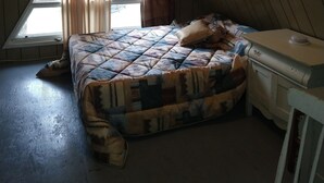 A bedroom with a sloped ceiling, a bed with a patterned quilt, a bedside table, and a window with curtains.