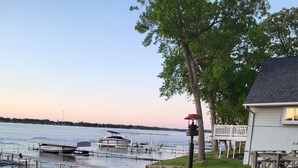 A patio with blue Adirondack chairs and a fire pit, overlooking a lake with boats docked. - Cozy Lake Front Cabin - East Lake Private Dock - GREAT LOCATION Next to The Ritz (Arnolds Park)