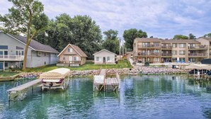 A lakeside property with a dock, a small house, and a larger building with balconies. - Cozy Lake Front Cabin - East Lake Private Dock - GREAT LOCATION Next to The Ritz (Arnolds Park)