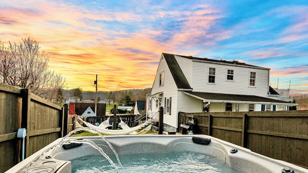A hot tub with water flowing, surrounded by a wooden fence, with a house and a sunset in the background. - Lux 4br 3ba, hot tub, stargazing, HUGE gameroom, 10 min to Summersville Lake (Summersville)